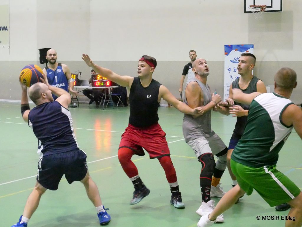 Grupa mężczyzn gra w koszykówkę w hali.