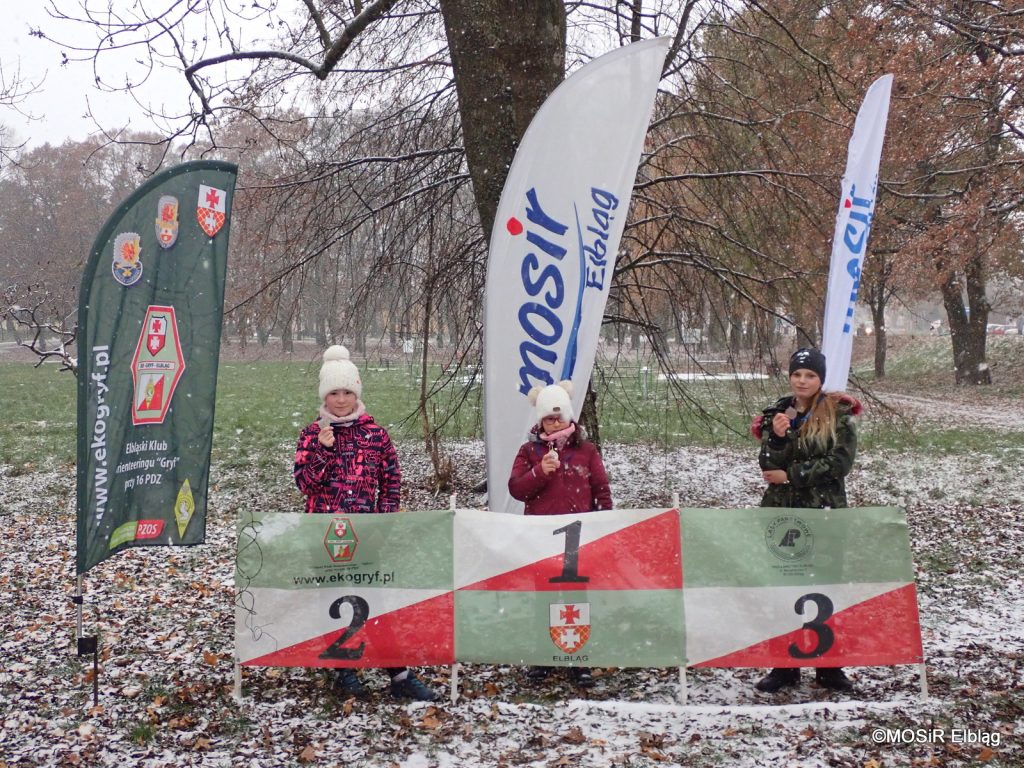 Troje dzieci stoi z medalami w parku